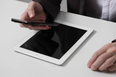 İş adamı beyaz masada tabletle akıllı telefon kullanıyor, yakın plan. Modern teknoloji