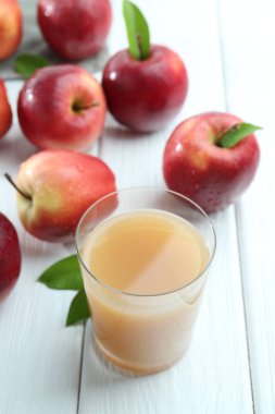 Bardakta elma suyu, beyaz ahşap masada meyveler.