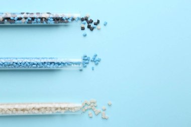 Açık mavi arka planda test tüplerinde renkli plastik granüller. Metin için boşluk