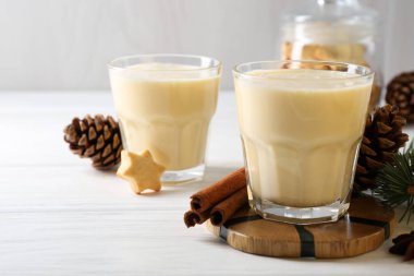Lezzetli Noel kokteyli (eggnog) bardaklarda, kozalaklarda ve beyaz ahşap masadaki baharatlarda, yakın plan