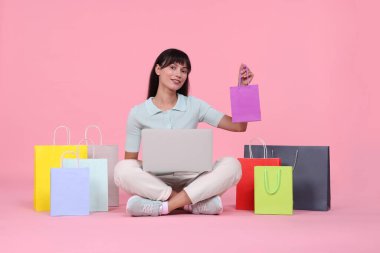 İnternet alışverişi. Dizüstü bilgisayarı ve pembe arka planda renkli çantaları olan mutlu kadın.