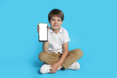 Açık mavi arka planda akıllı telefonu olan şirin bir çocuk.