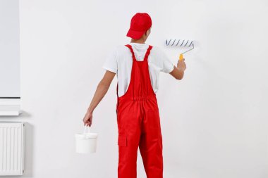 Erkek tamirci duvarları boyuyor, içeride patenli, arka manzaralı.