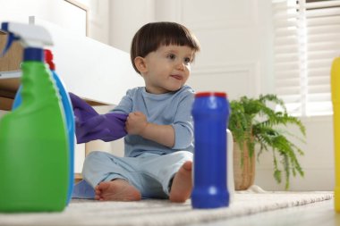Evdeki dolabın yanındaki deterjan şişelerinin arasında eldivenle oynayan küçük çocuk. Çocuk tehlikede.