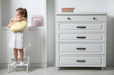 Little girl with toy standing on step stool indoors, space for text clipart