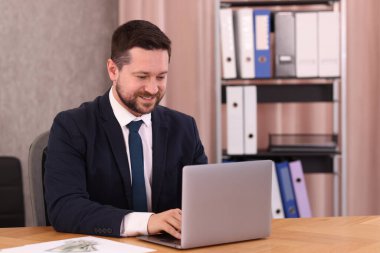 Banker ofisteki ahşap masada dizüstü bilgisayarla çalışıyor.