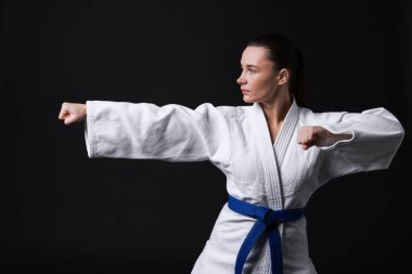 Kimonolu genç bir kadın siyah arka planda karate yapıyor.