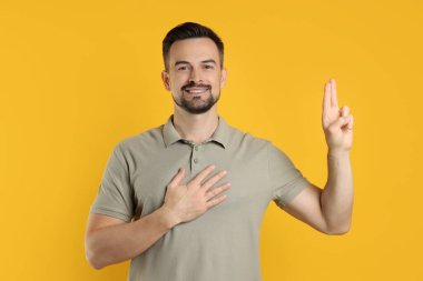 Turuncu arka planda yemin işareti gösteren bir adam. Söz veriyorum.