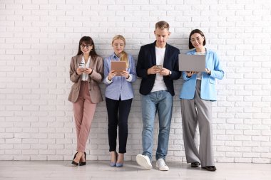 Beyaz tuğlalı duvarın yanında farklı aletler kullanan bir grup insan. Modern teknoloji