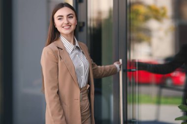 Şık takım elbiseli gülen kadın açık hava ticaret merkezinin kapısını açıyor.
