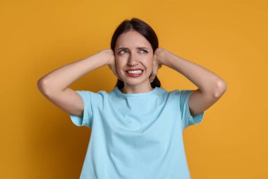 Woman covering her ears on orange background clipart