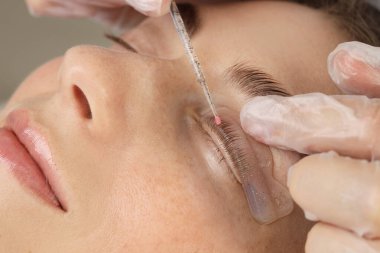 Kirpik kaplama prosedürü. Estetisyen kadın kirpiklerini güzellik salonundaki pede yapıştırıyor.