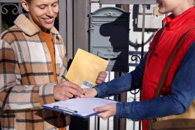 Man signing papers while receiving parcel from postwoman outdoors, closeup clipart