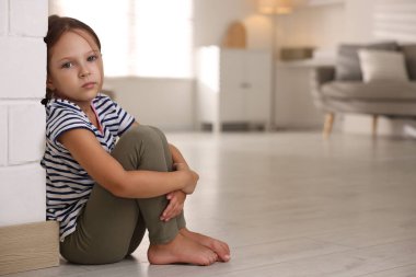 Orphanage concept. Sad girl sitting on floor indoors clipart