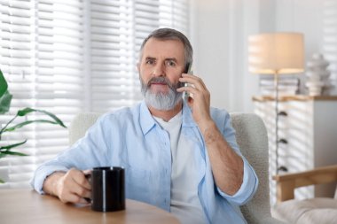 Elinde bir bardak içki olan son sınıf öğrencisi kapalı bir masada akıllı telefondan konuşuyor.
