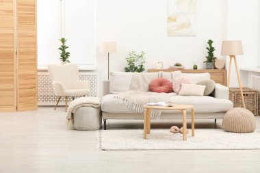 Oturma odasının içi aydınlık. İçinde battaniye ve diğer mobilyalar olan rahat bir kanepe.