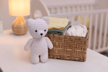 Çocuk kıyafetleri ve oyuncak ayılarla dolu bir sepet. Beyaz ahşap masa içinde, yakın plan.