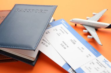 Seyahat acentesi. Uçuş biletleri, pasaportlar ve turuncu arka plandaki uçak modeli, yakın plan.