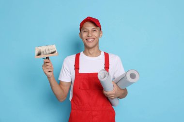 Açık mavi zemin üzerinde fırça ve rulo duvar kağıdı ile genç dekoratör