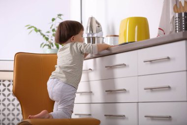 Küçük çocuk mutfakta tost makinesiyle oynuyor. Tehlikeli bir durum.