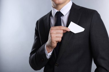 Gri arka planda ceketinin cebinden boş kartvizit alan adam, yakın plan. Tasarım için model