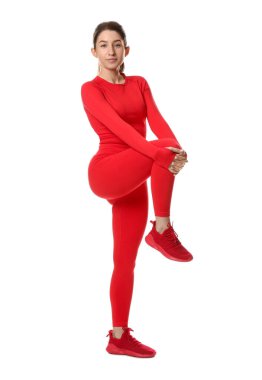 Spor giyimli bir kadın beyaz arka planda egzersiz yapıyor.