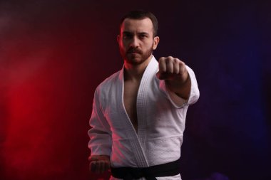 Üniformalı bir adam renkli ışıklarla ve dumanla karate yapıyor.