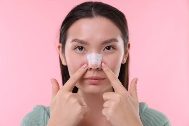 Woman with medical bandage on her nose after plastic surgery operation against pink background clipart