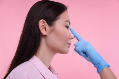 Doktor pembe arka plandaki estetik ameliyattan sonra hastanın burnunu kontrol ediyor.