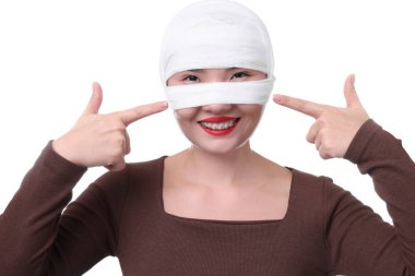 Beyaz arka plandaki estetik ameliyattan sonra burnu tıbbi bandaja sarılı bir kadın.