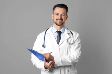 Steteskop ve gri arka planda panosu olan gülümseyen bir doktor.