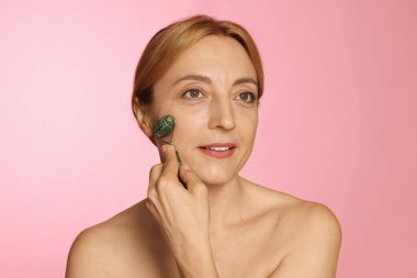 Güzel bir kadın pembe arka planda kendi kendine masaj yapıyor.