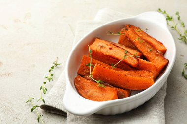 Lezzetli pişmiş tatlı patates parçaları fırın kabında hafif desenli masada mikro yeşillikler.