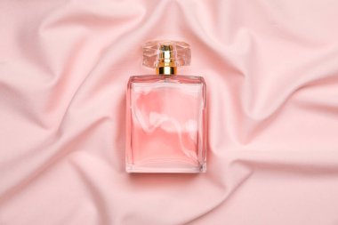 Bottle of perfume on pink silk fabric, top view clipart