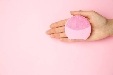 Kadının elinde pembe arka planda yüz temizleme fırçası var. Metin için boşluk