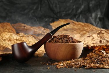 Tütün, kurumuş yapraklar ve siyah masada tüttürme piposu. Yakın plan.