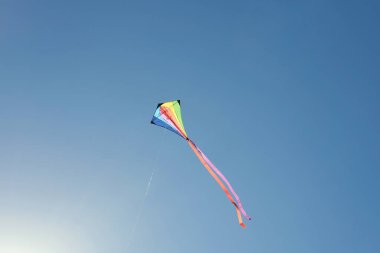 Güneşli bir günde mavi gökyüzünde uçan renkli bir uçurtma