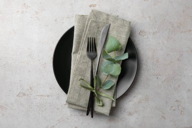 Siyah tabak, çatal bıçak, peçete ve okaliptüs dalı gri desenli masa, üst görünüm