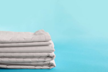 Stacked clean bed linens on light blue background, space for text