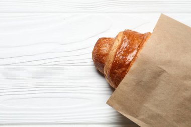 Beyaz ahşap masanın üstünde taze kruvasan olan kağıt torba, üst manzara. Metin için boşluk