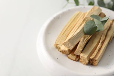 Palo Santo çubukları ve okaliptüs yaprakları beyaz masada, yakın plan. Metin için boşluk