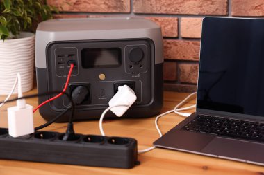 İçerideki ahşap masada taşınabilir elektrik santralinden dizüstü bilgisayar şarj ediliyor.