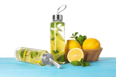 Şişe içinde naneli limon suyu, yapraklar ve açık mavi ahşap masada beyaz arka planda taze meyveler.