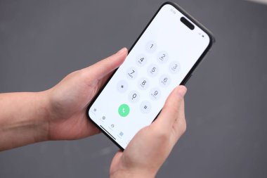 Tuşlayıcı uygulamalı akıllı telefon tutan kadın bulanık gri arkaplan, yakın plan