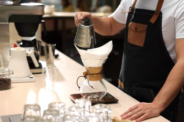 Barista kahve makinesinde kahve yapıyor. Kafedeki masada kağıt filtresi var. Yakın plan.