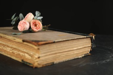 Eski kitap, güzel çiçekler ve okaliptüs dalları koyu dokulu masa, yakın çekim.