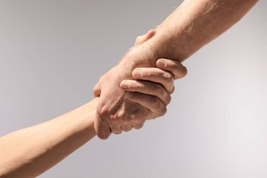 Yardım ve destek. Açık gri arka planda el ele tutuşan insanlar, yakın plan.