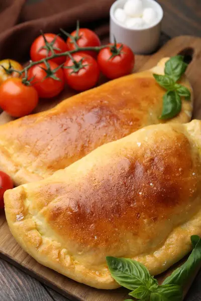 Ahşap masada fesleğen, domates ve mozzarella peynirli lezzetli vejetaryen calzones, yakın plan.