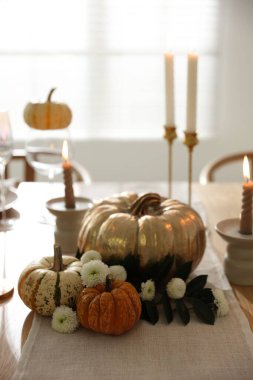 Yemek odasında mum ve sonbahar dekoru olan şık bir masa.