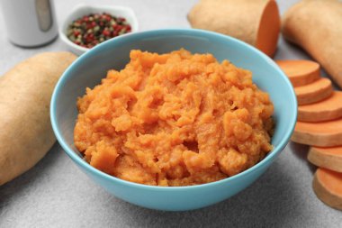 Tatlı patates püresi kasede ve taze sebzeler gri masada, yakın plan.